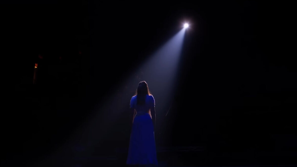 Jenna stands in a spotlight in a frame from Waitress The Musical